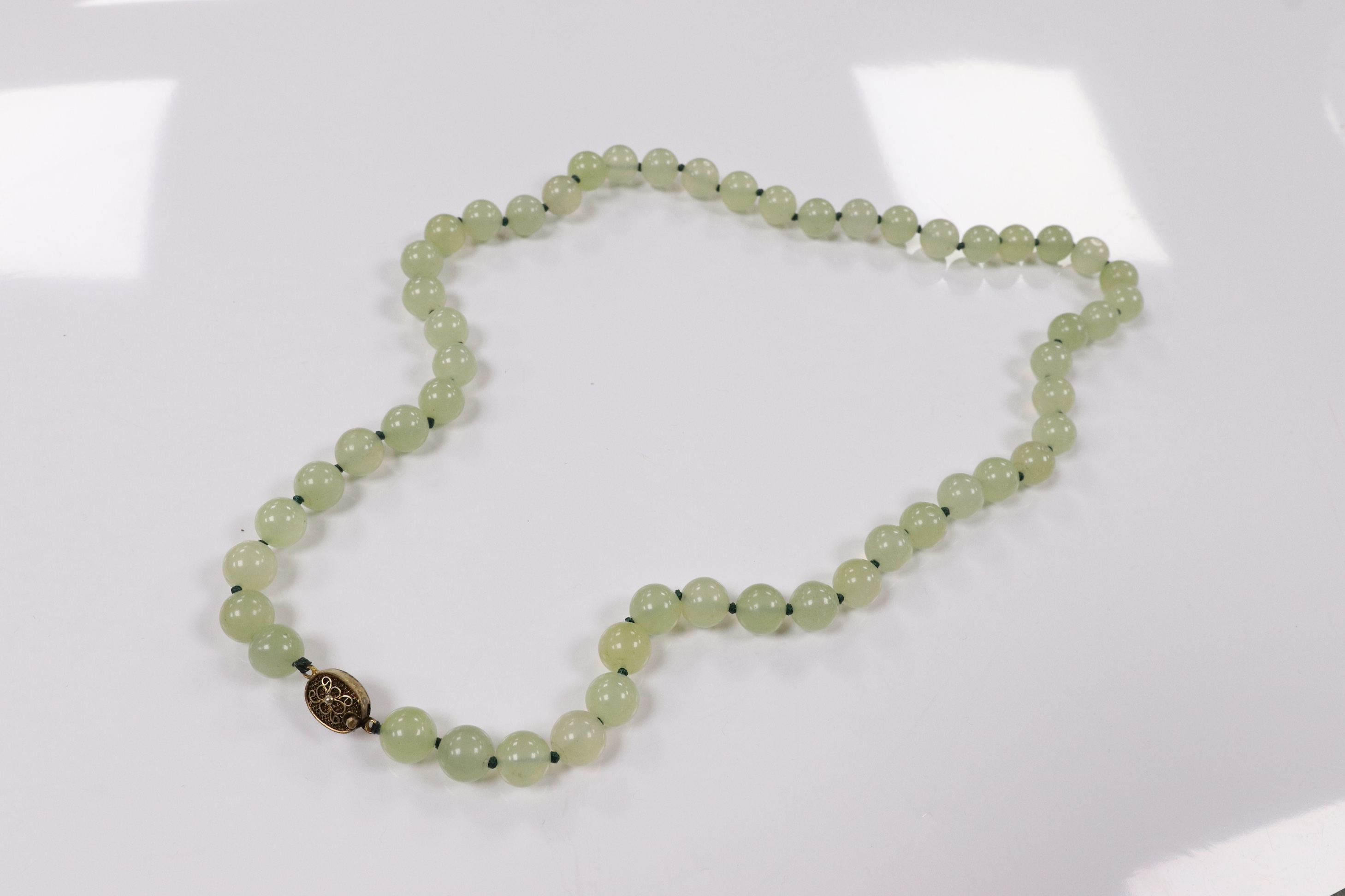 A single strand simulated jade bead necklace, with a gilt metal filigree clasp, 58cm. Condition - fair